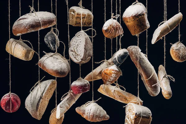 Pain blanc et brun et pâtisserie suspendus sur des cordes isolées sur noir — Photo de stock