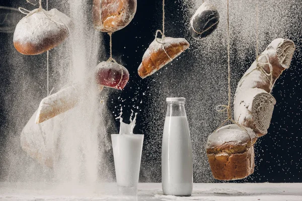 Milch spritzt im Glas auf den Tisch und vier fallen auf Brot, das an Schnüren hängt, isoliert auf schwarz — Stockfoto