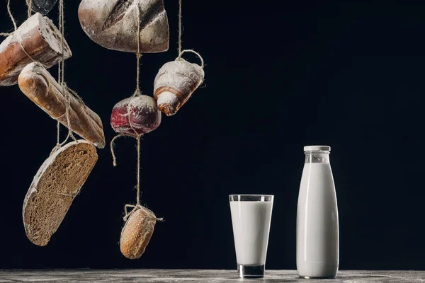 Milk on table and bread with flour hanging on strings isolated on black with copy space — Stock Photo