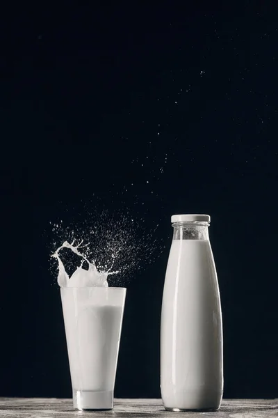 Salpicaduras de leche fresca en vidrio cerca de botella aislado en negro - foto de stock