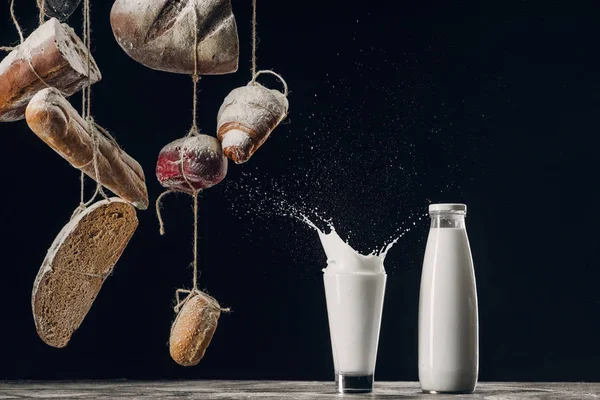 Pan casero colgando de las cuerdas cerca de salpicar la leche aislado en negro - foto de stock