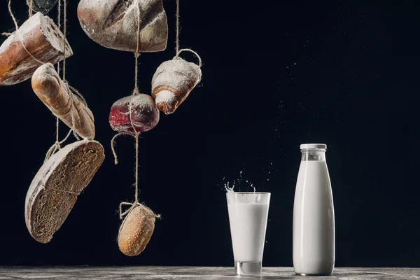 Homemade bread hanging on ropes near milk isolated on black — Stock Photo