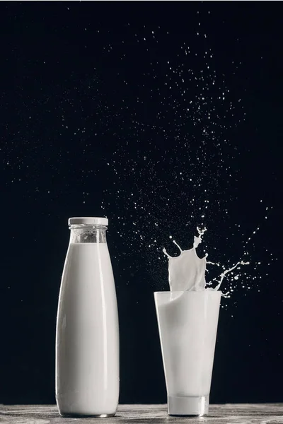 Splashing milk in glass near bottle isolated on black — Stock Photo