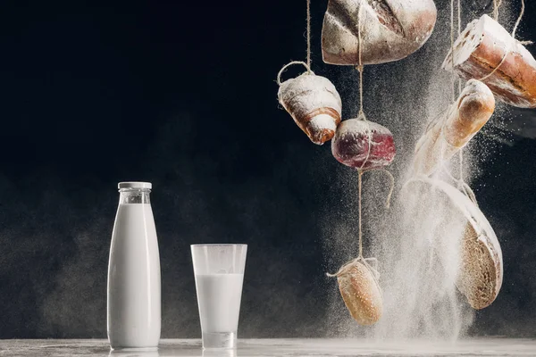 Mehl, das auf selbstgebackenes Brot fällt, hängt an Seilen in der Nähe von Spritzmilch auf Schwarz mit Kopierraum — Stockfoto