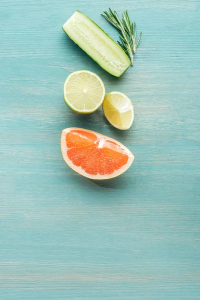 Vue de dessus des fruits coupés, du concombre et du romarin sur une surface texturée bleue — Photo de stock