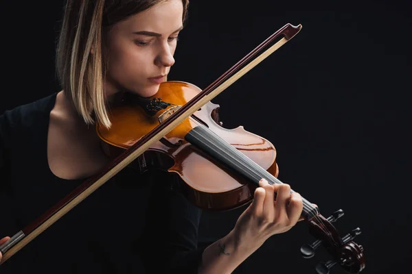 Joven mujer concentrada tocando violonchelo con arco aislado en negro - foto de stock