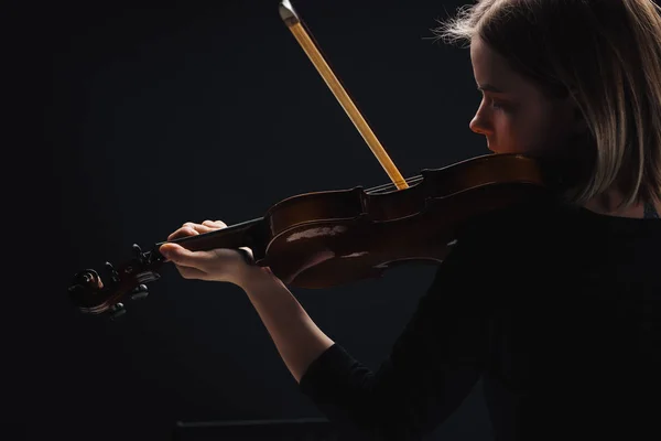 Jeune femme concentrée jouant du violoncelle avec arc dans l'obscurité isolé sur noir — Photo de stock