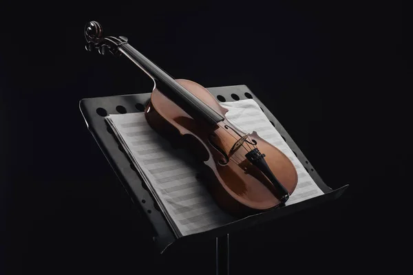 Classic wooden cello on opened music book on stand isolated on black — Stock Photo