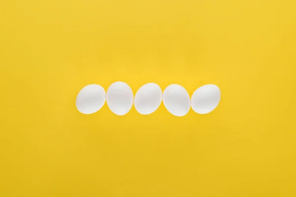 Five white chicken eggs in row on yellow background — Stock Photo