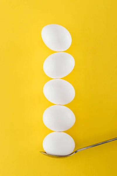 Five white chicken eggs on spoon on yellow background — Stock Photo