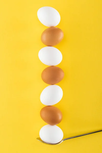 Seven white and brown chicken eggs on spoon on yellow background — Stock Photo