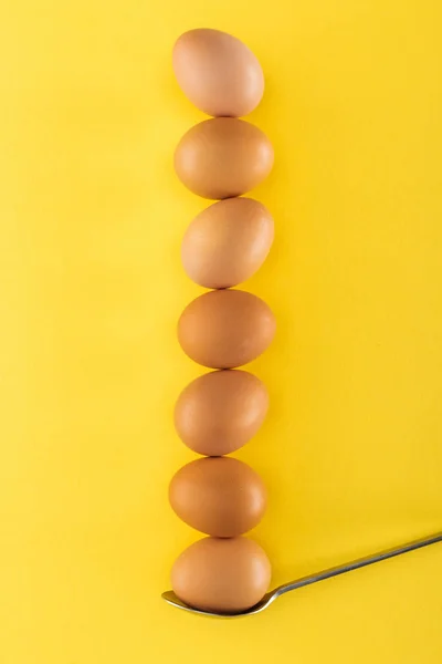 Seven brown chicken eggs on spoon on yellow background — Stock Photo