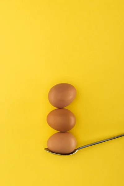 Three brown chicken eggs on spoon on yellow background — Stock Photo