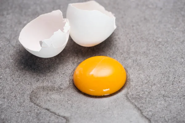 Nahaufnahme von rohem zertrümmertem Ei mit Eigelb und Eiweiß auf grauem, strukturiertem Hintergrund — Stockfoto