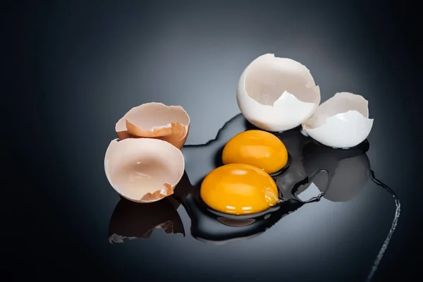 Raw smashed chicken eggs with yolks, proteins and eggshell on black background — Stock Photo