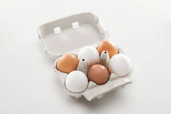 Huevos de gallina crudos blancos y marrones en caja de cartón sobre fondo blanco - foto de stock