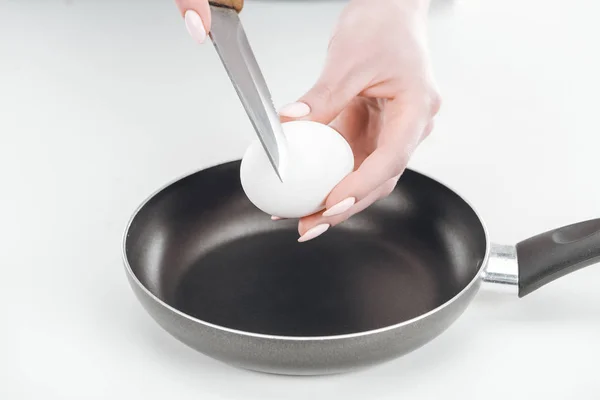 Обрізаний вид жінки, що тримає куряче яйце і ніж біля сковороди на білому тлі — стокове фото