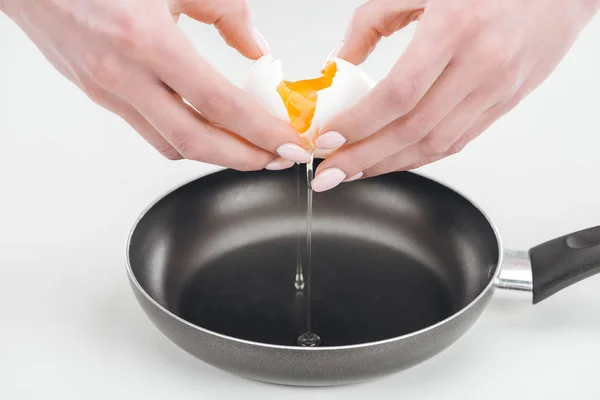 Vue partielle de la femme fracassant oeuf avec les mains dans la casserole sur fond blanc — Photo de stock