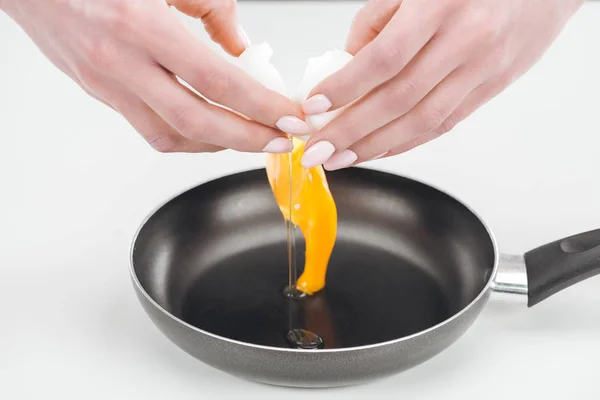 Cropped view of woman smashing chicken egg into pan on white background — Stock Photo