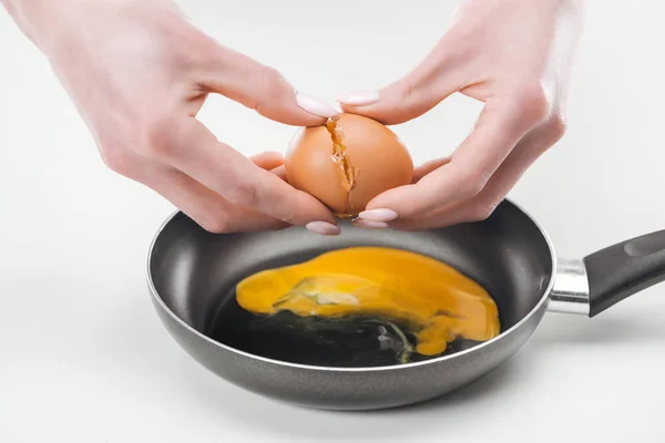 Vue recadrée de la femme fracassant oeuf de poulet tout en préparant des œufs brouillés dans une casserole sur fond blanc — Photo de stock