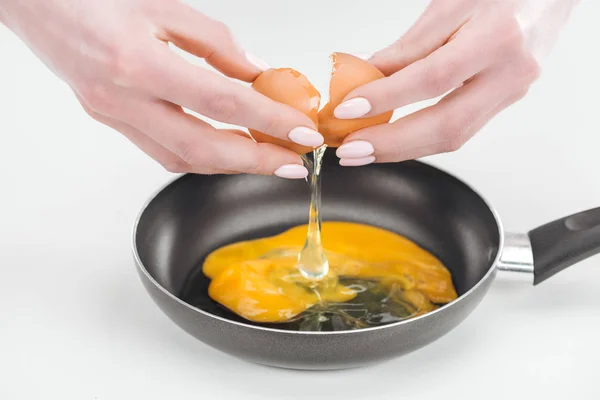 Vue recadrée de la femme casser des œufs tout en préparant des œufs brouillés dans une casserole sur fond blanc — Photo de stock