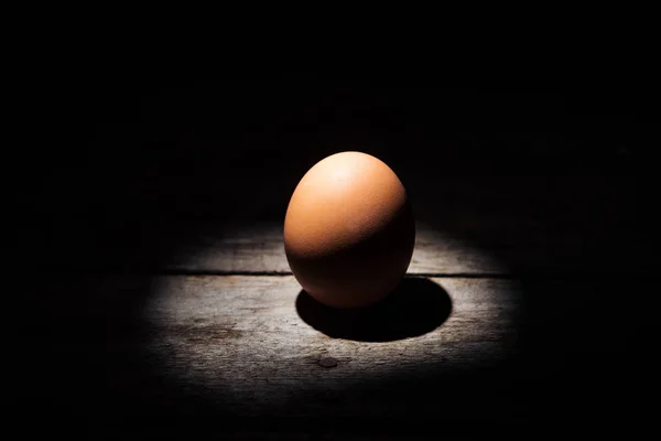 Ovo de galinha marrom na escuridão na superfície de madeira intemperizada — Fotografia de Stock