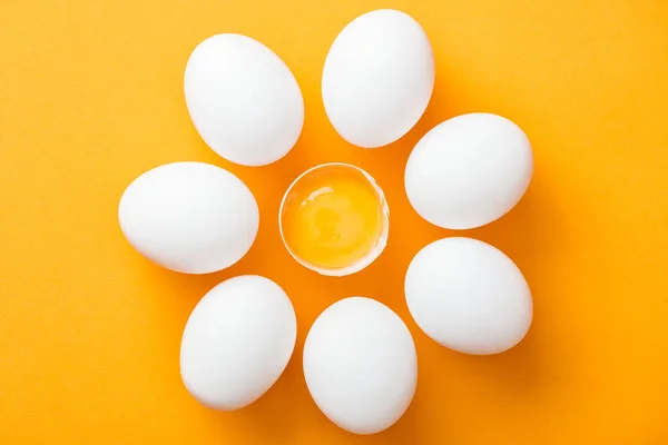 Draufsicht auf ganze weiße Eier und zertrümmertes mit Eigelb auf leuchtend orangefarbenem Hintergrund — Stockfoto