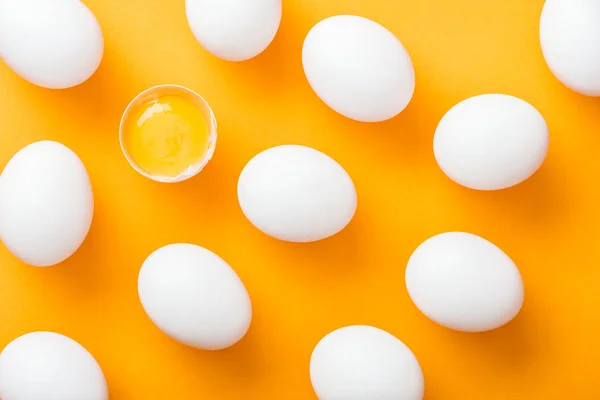 Vista superior de huevos de pollo frescos blancos enteros con uno aplastado sobre fondo naranja brillante - foto de stock