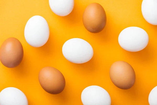 Vue de dessus des oeufs de poulet frais blancs et bruns entiers sur fond orange vif — Photo de stock