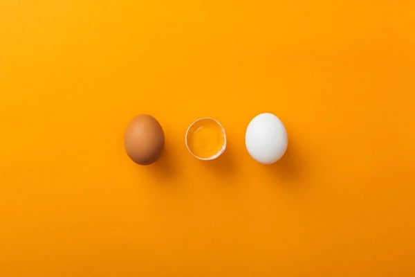 Top view of two whole chicken eggs with smashed one on bright orange background — Stock Photo