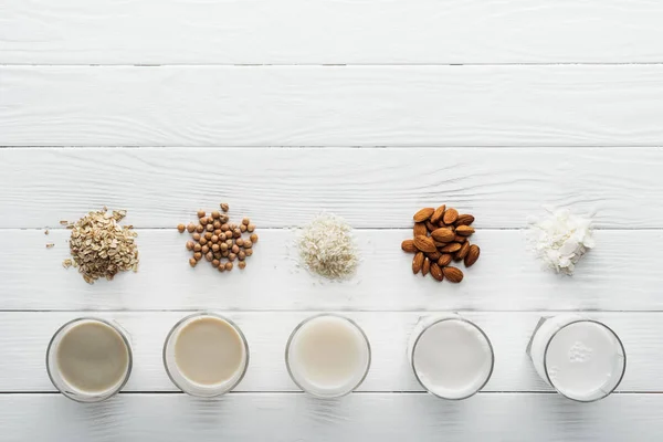 Top view of glasses with coconut, chickpea, oat, rice and almond milk on white wooden table with ingredients — Stock Photo