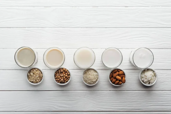 Top view of glasses with coconut, chickpea, oat, rice and almond milk with ingredients in bowls — Stock Photo