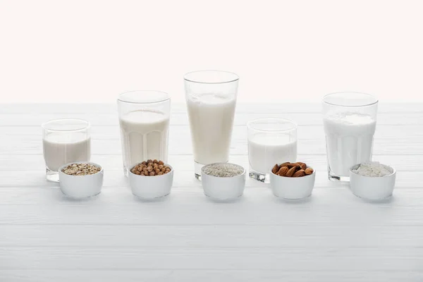 Glasses with coconut, chickpea, oat, rice and almond milk with ingredients in bowls isolated on white — Stock Photo