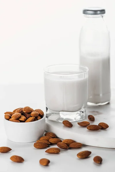 Миндальное молоко в бутылке и стекло возле орехов в миске изолированы на белом — стоковое фото