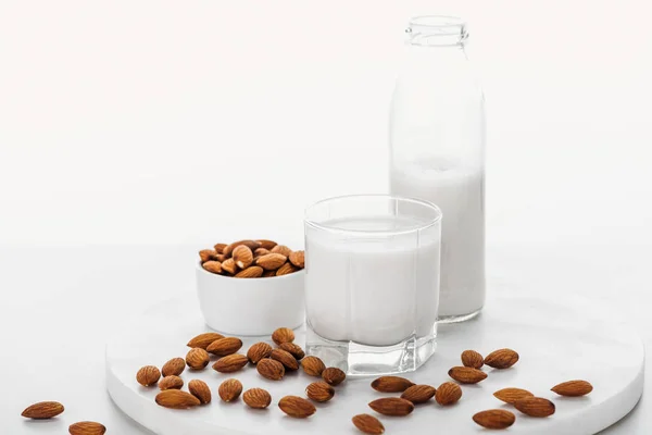 Веганське біле мигдалеве молоко в пляшці і склянці біля горіхів в мисці ізольовано на білому — стокове фото