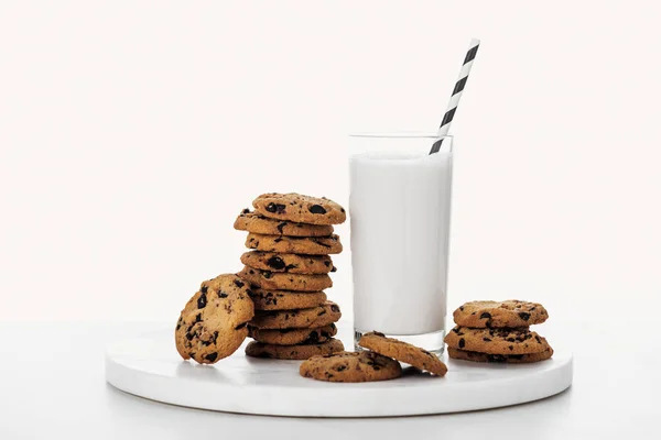 Pila de sabrosas galletas de chocolate cerca de vidrio con leche y paja aislada en blanco - foto de stock