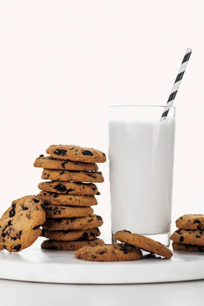 Mucchio di deliziosi biscotti al cioccolato vicino al vetro con paglia e latte isolato su bianco — Foto stock