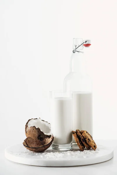 Leche vegana de coco en vidrio y botella cerca de galletas de coco y chocolate aisladas en blanco - foto de stock