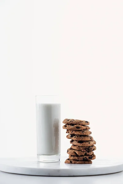 Leche fresca en vaso cerca de galletas de chocolate sobre soporte de mármol aislado en blanco - foto de stock