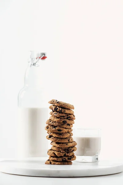 Lait frais en verre et bouteille près de biscuits au chocolat sur support en marbre isolé sur blanc — Photo de stock
