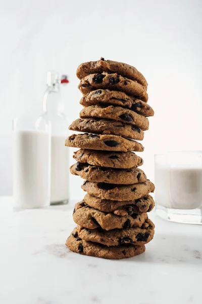 Focalizzazione selettiva di biscotti al cioccolato vicino bottiglia e bicchieri con latte sul tavolo di marmo — Foto stock
