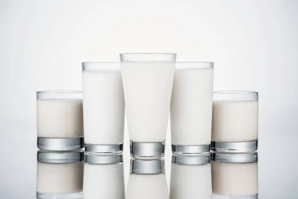 Gläser mit Bio-Alternativmilch auf grauem Hintergrund mit Reflexion — Stockfoto