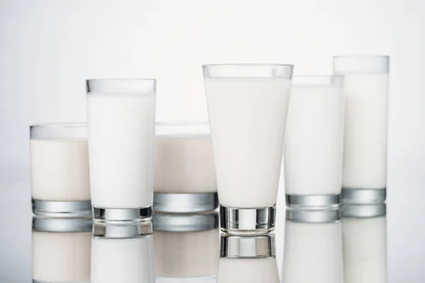 Стаканы с органическим свежим альтернативным молоком на сером фоне с отражением — стоковое фото