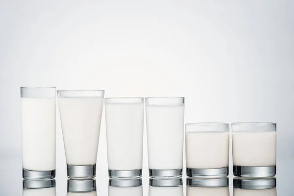 Row of glasses with organic vegan milk on grey background — Stock Photo