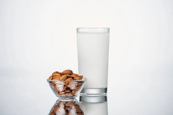 Mandel vegane Milch im Glas neben Schüssel mit Nüssen auf grauem Hintergrund — Stockfoto