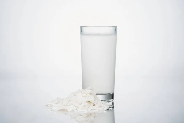 Coconut vegan milk in glass near coconut slices on grey background — Stock Photo