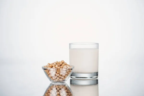 Pois chiche lait végétalien en verre près du bol avec haricots sur fond gris — Photo de stock