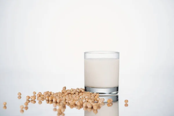 Pois chiche lait végétalien en verre près de haricots épars sur fond gris — Photo de stock