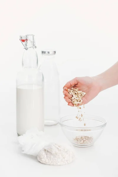 Vista recortada de la mujer poniendo copos de avena en un tazón mientras cocina la leche vegana de avena - foto de stock