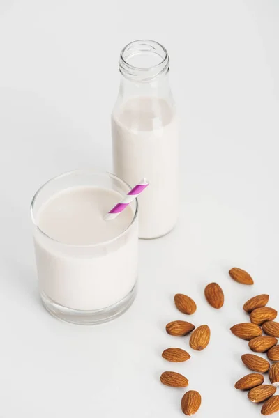 Leche de almendras orgánica en botella y vaso con paja cerca de almendras dispersas - foto de stock